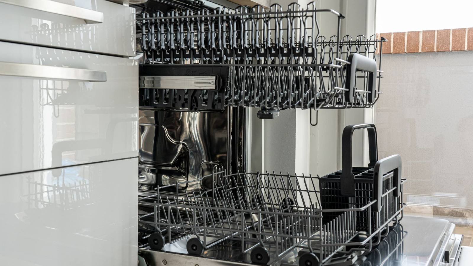 Open built-in dishwasher with empty racks in a sunny kitchen